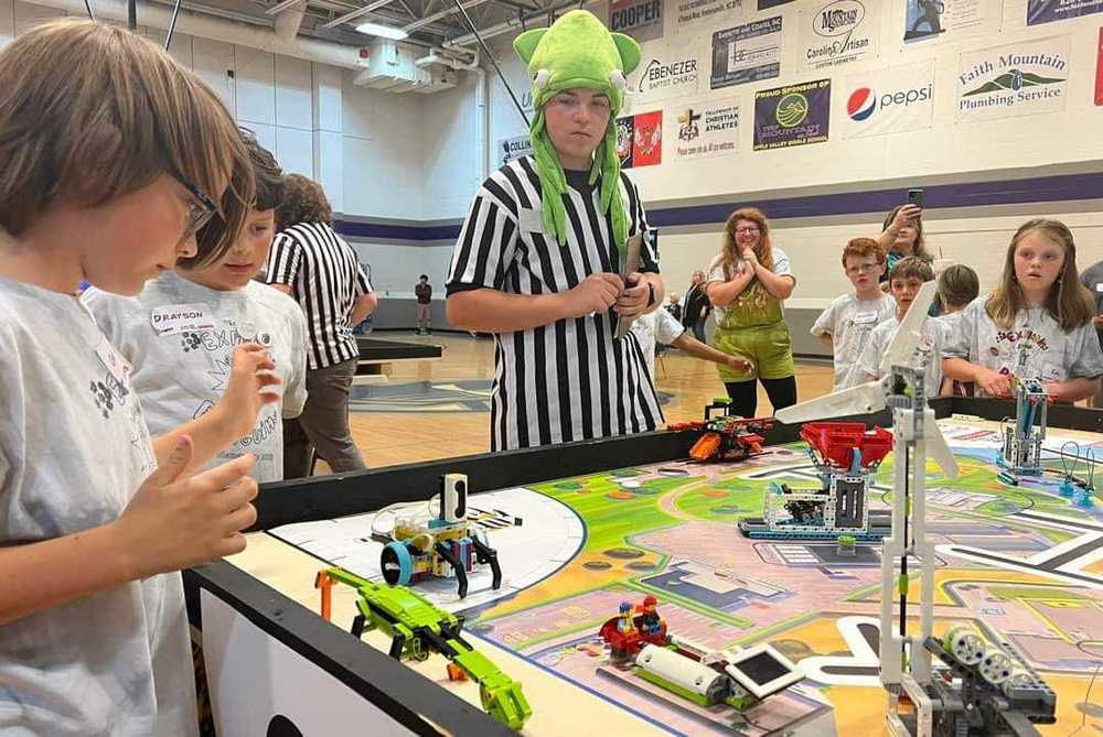 Photograph of robotics competition with referee looking at student's robots on a table