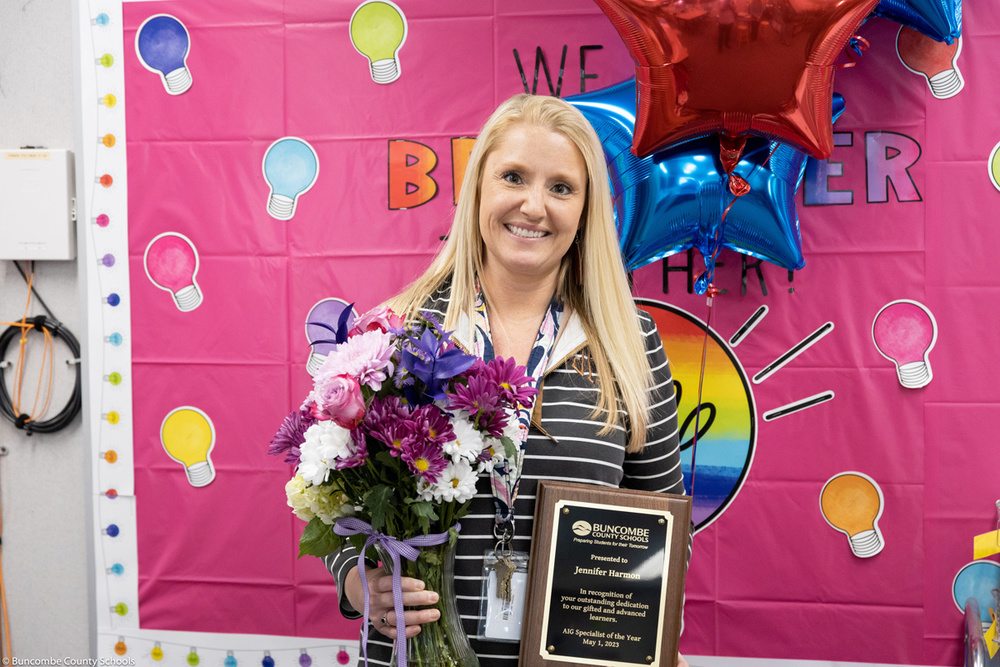 Jennifer Harmon poses while holding  a plaque, flowers, and balloons.