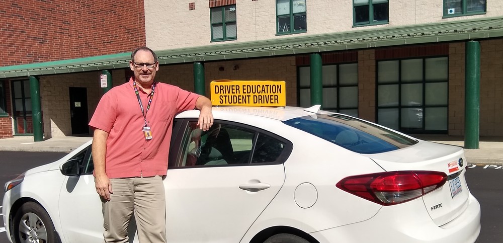 A picture of Mr. McEntire with a white drivers ed car