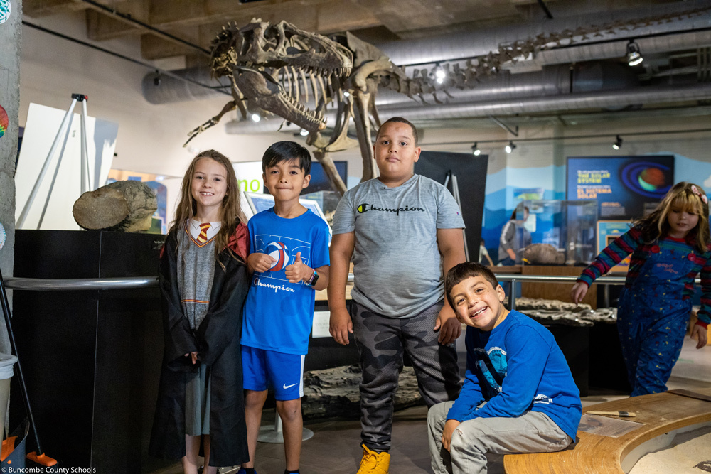 Four second graders pose in front of a dinosaur skeleton at Asheville Museum of Science.