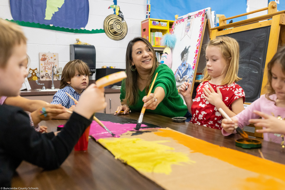 Sandra Forero helps her students paint a cardboard airplane.