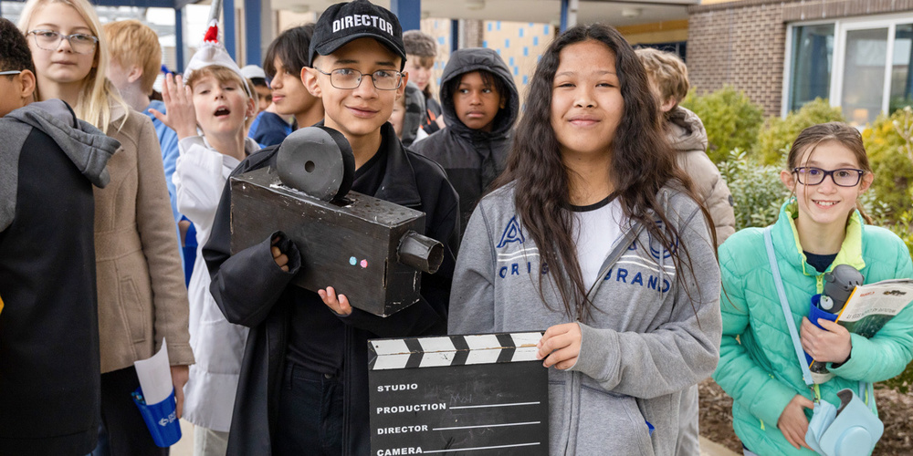 Two students pose while holding filmmaking props.