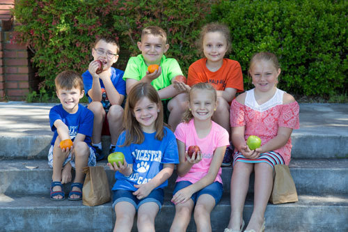 Seven students sitting outside on steps enjoying a healthy snack together