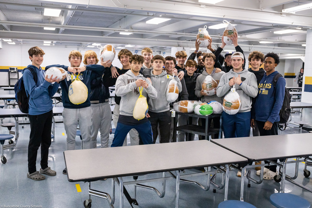 The baseball team holds frozen turkeys in the T.C. Roberson High cafeteria.