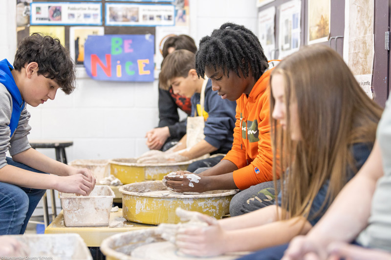 Students work at potter's wheels.
