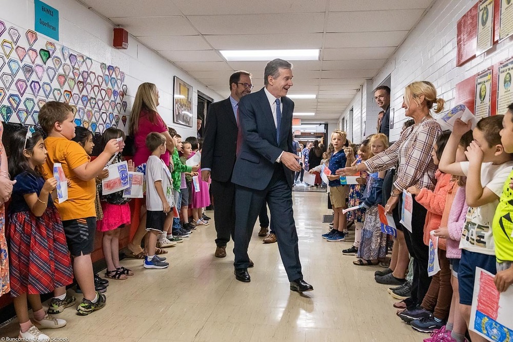 Gov. Cooper reaches out to shake a teacher's hand while walking down the hall at Weaverville Primary.