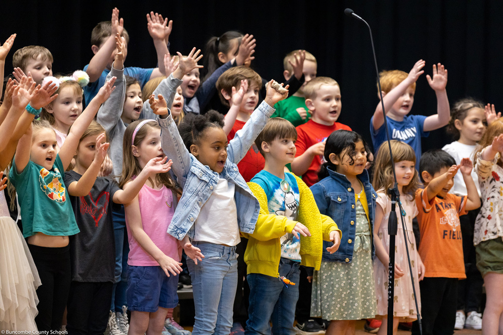 Kindergarteners throw up their hands as they sing a song.