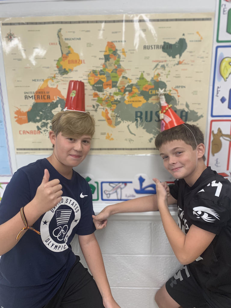 Students pose with their custom hats in front of world map