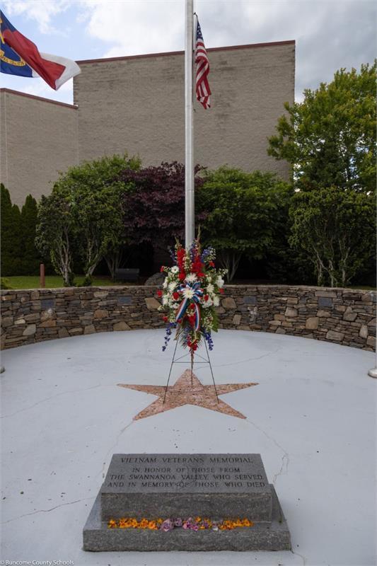 Vietnam veterans memorial monument in front of flag pole and flower arrangement