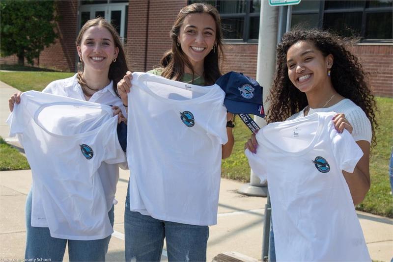 Three students holding matching t-shirts
