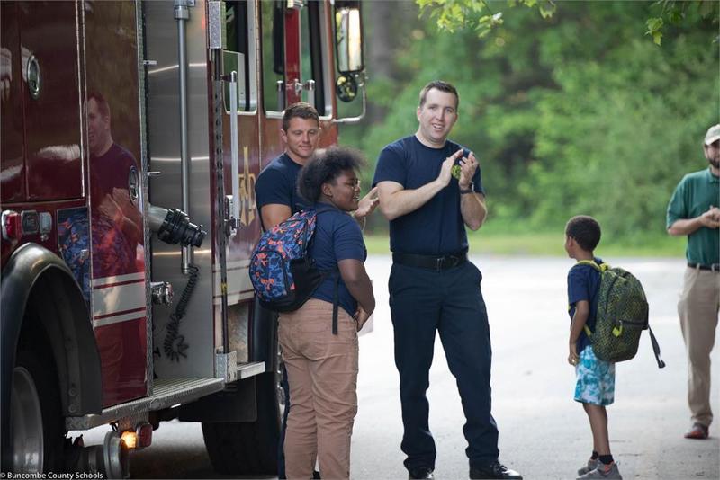 students and fire fighters standing in front of a fire truck