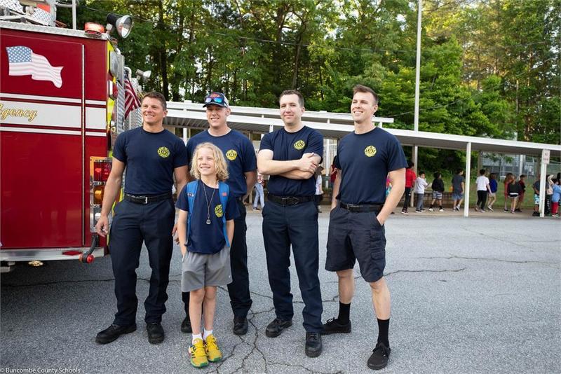 Student standing in front of a fire truck with 4 fire fighters