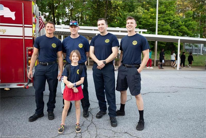 Student standing in front of a fire truck with 4 fire fighters