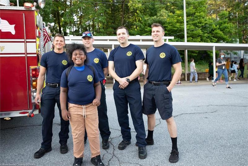 Student standing in front of a fire truck with 4 fire fighters