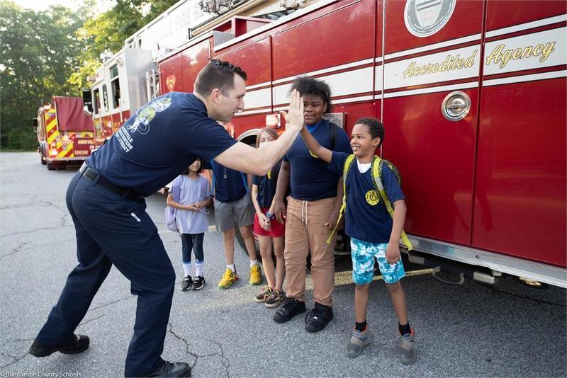 Fire fighter high fiving a student near other students in front of fire truck