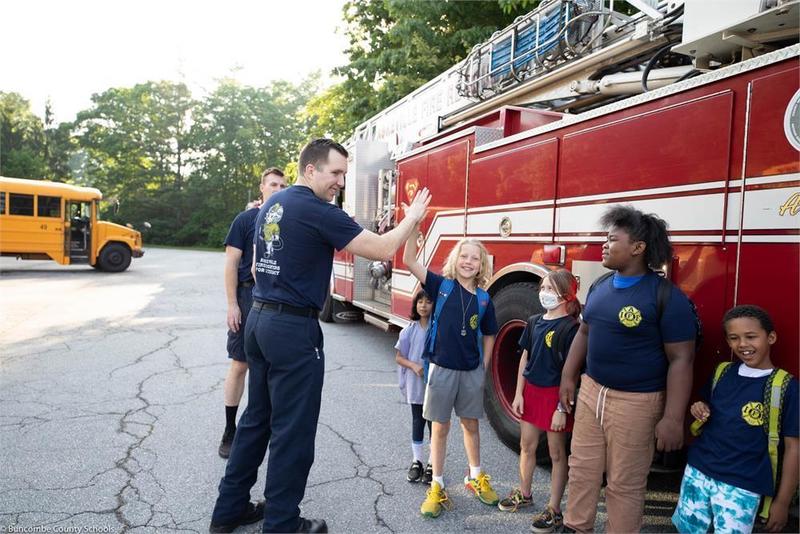 Fire fighter high fiving a student near other students in front of fire truck