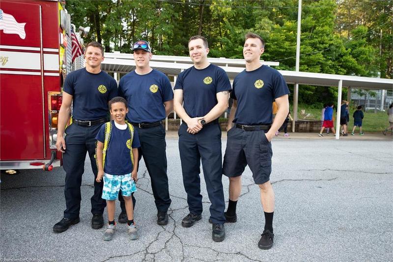 Student standing in front of a fire truck with 4 fire fighters