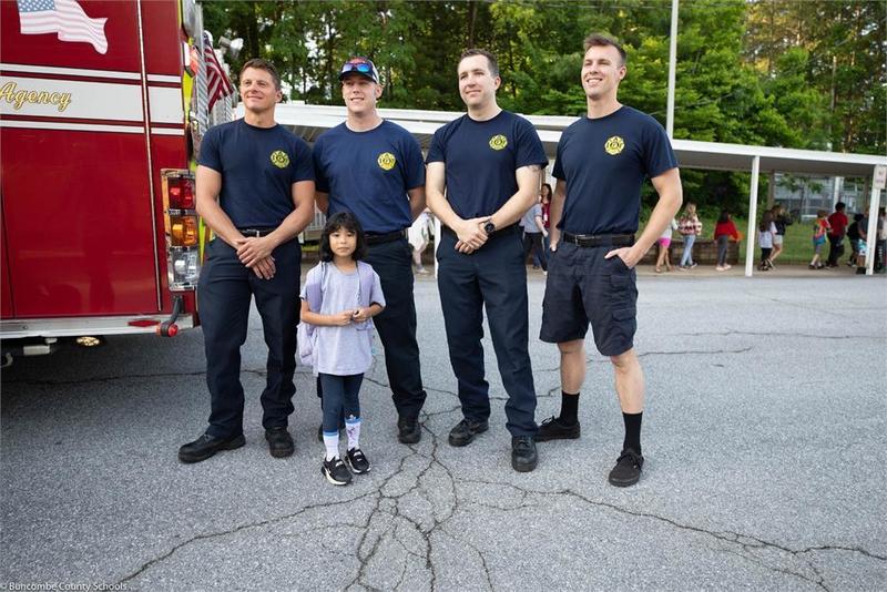 Student standing in front of a fire truck with 4 fire fighters