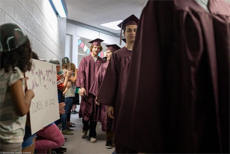 Graduates walking down the hall past younger students holding signs