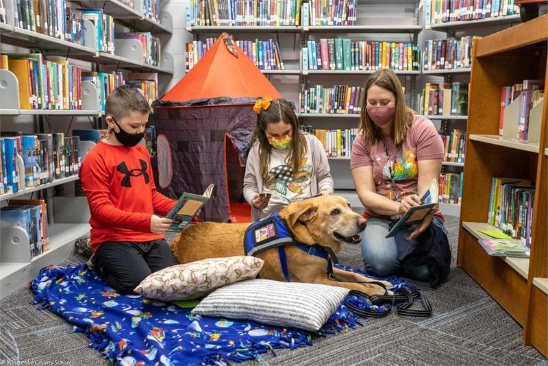 Students read with therapy dog on pillows in center