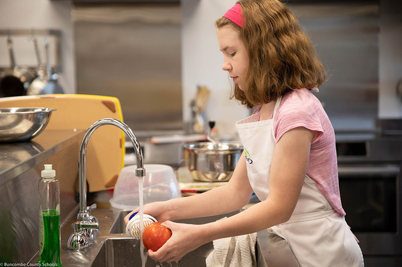 Student washing a ripe tomato that will become part of the homemade pizza