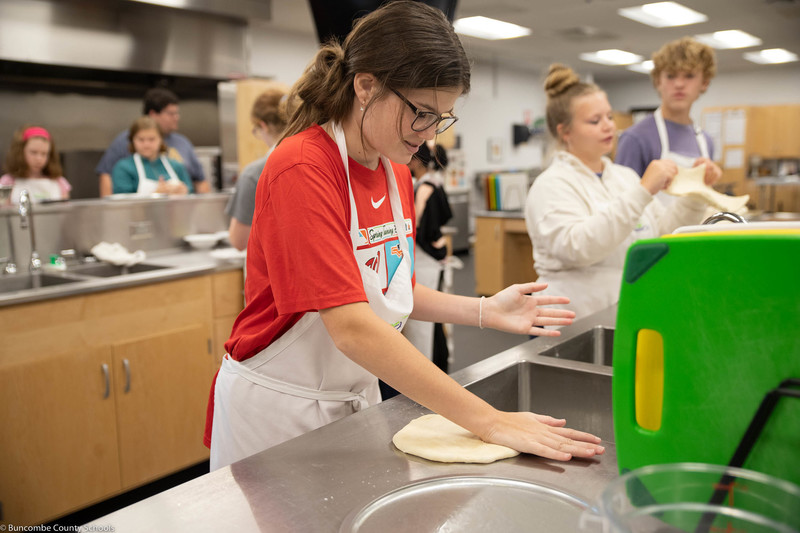 Student pressing out the dough for her pizza. 