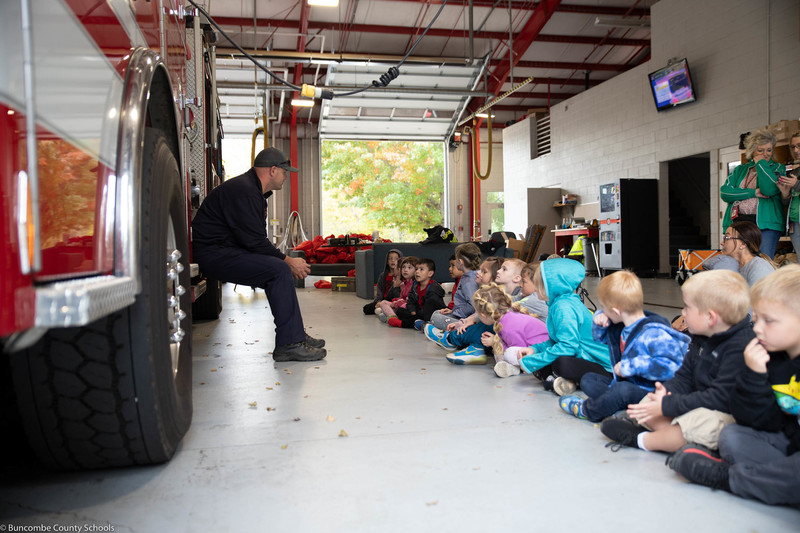 Students listening to a firefighter as the sit in front of a truck.